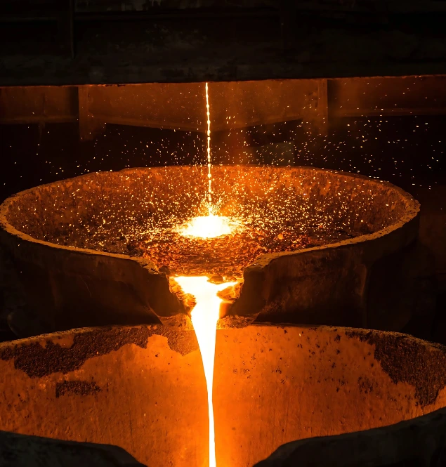 Molten metal pouring into casting molds inside a steel foundry with sparks flying